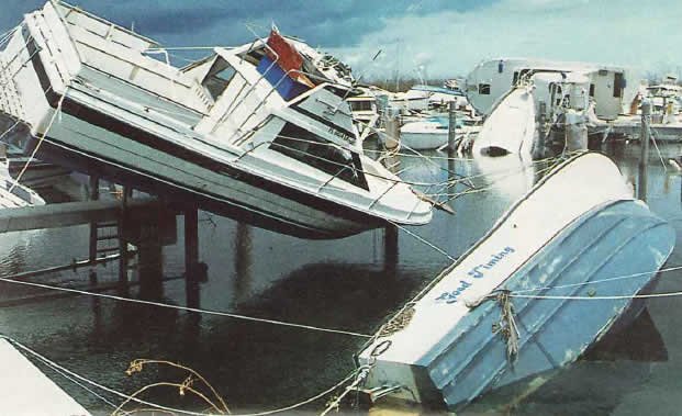 A boat injured by a Hurricane is suspended from a dock by a few docklines.
