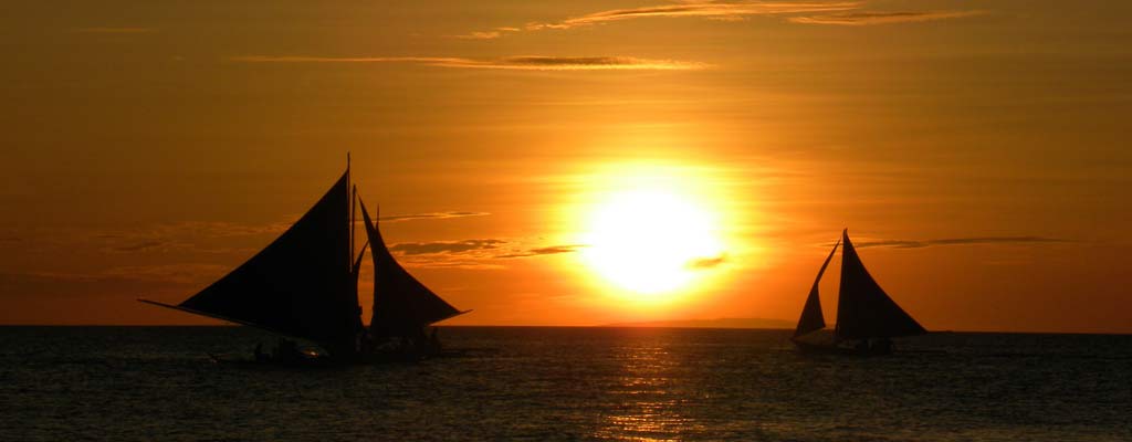 two sailboats pass eachother in front of sunset