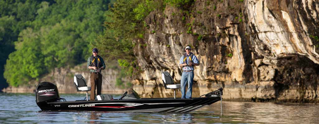 two men standing on a flatbed fishing boat, on a lake near a small, wooded cliff