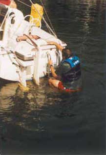 A person in a life jacket re-boarding a sailboat from the transom.