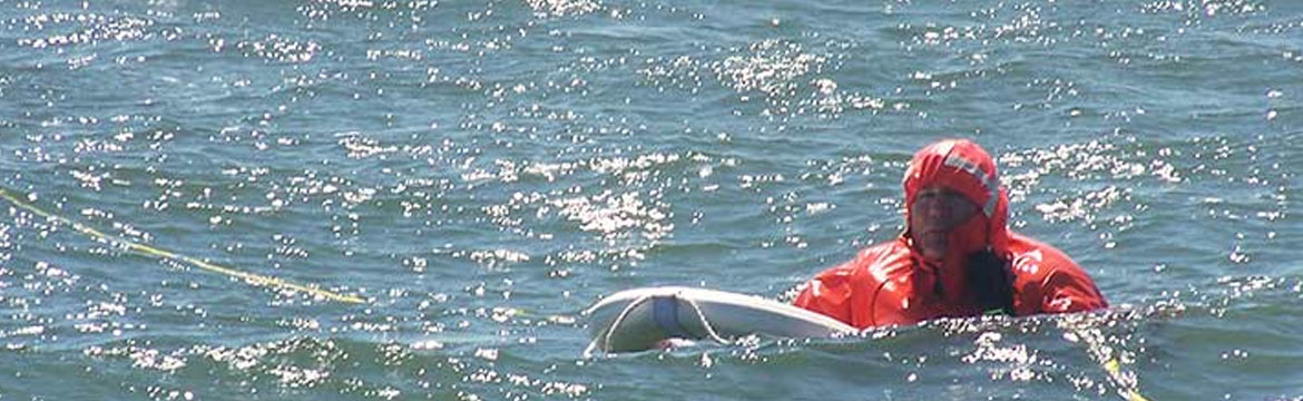 a man overboard, holding on to a flotation device as he waits to be pulled in