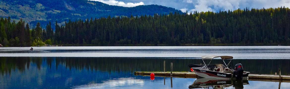 a boat sitting at dock on a beautiful lake with pine trees on hills