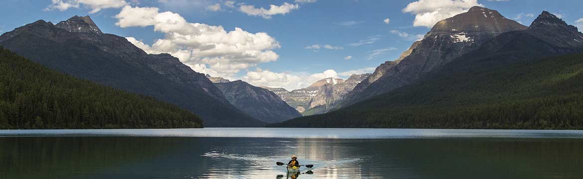a person kayaking on a lake with large mountains behind