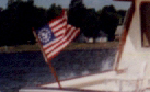 the aft flag of the above boat is blowing as if there is a wind coming from behind the boat